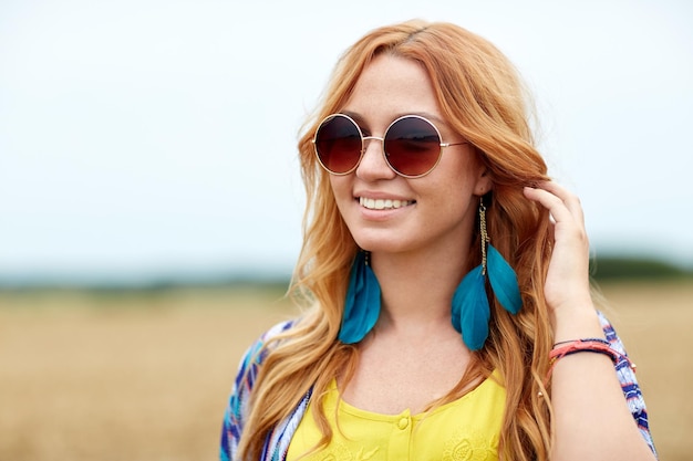 Natur, Sommer, Jugendkultur und People-Konzept - lächelnde junge rothaarige Hippie-Frau mit Sonnenbrille im Freien