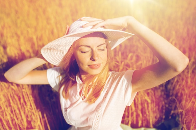 Foto natur, sommerferien, urlaub und personenkonzept - glückliche junge frau in weißem kleid und sonnenhut, die die sonne auf dem getreidefeld genießt