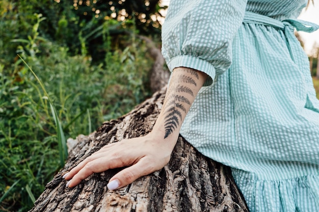 Naturaleza y mejorar la salud mental Mano de mujer con tatuaje de helecho en el tronco de un árbol en el bosque