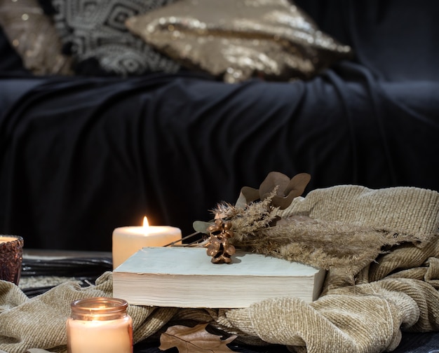 Naturaleza muerta en la mesa con velas, libro de suéter y hojas de otoño. Acogedora sala de estar, decoración interior del hogar.