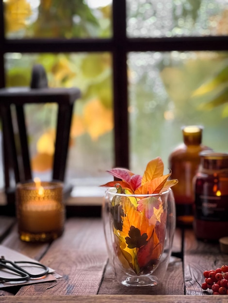 La naturaleza muerta de otoño de las hojas en un vaso en la ventana