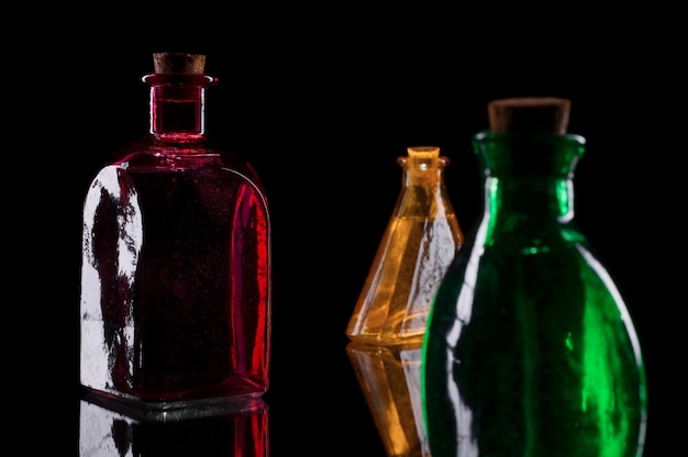 Naturaleza muerta de tres botellas decorativas de colores con tapones en vidrio contra un fondo negro