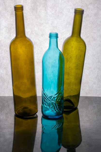 Foto naturaleza muerta con tres botellas de vidrio de colores sobre un fondo gris