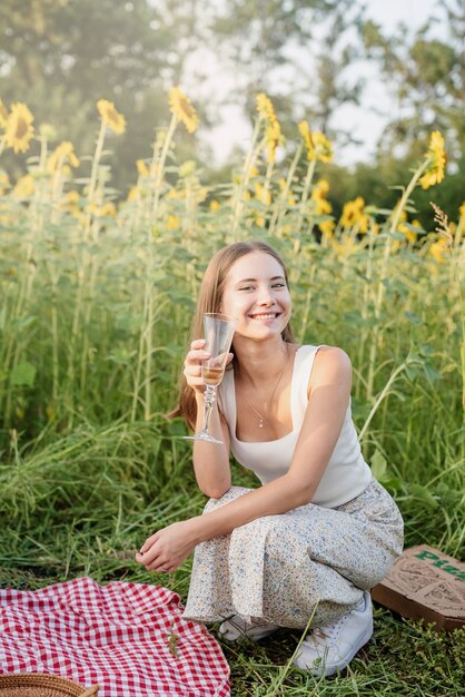 Foto naturaleza otoñal. diversión y mentira. joven adolescente haciendo un picnic en el campo de girasol en la puesta del sol bebiendo champán