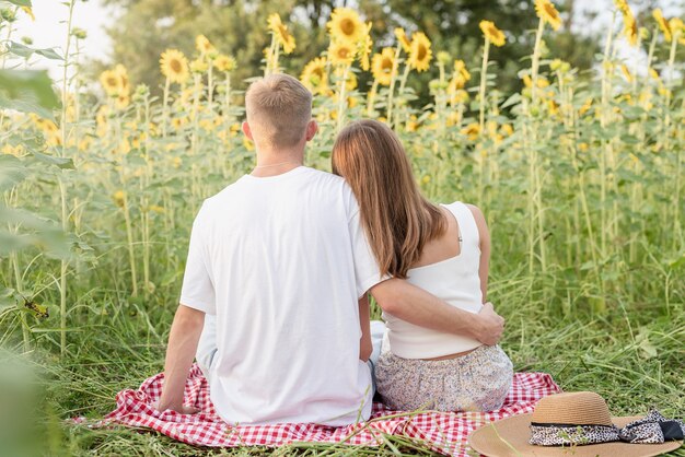 Foto naturaleza otoñal. diversión y mentira. picnic de la joven pareja de adolescentes en el campo de girasol en la puesta del sol, disfrutando del tiempo juntos, vista trasera