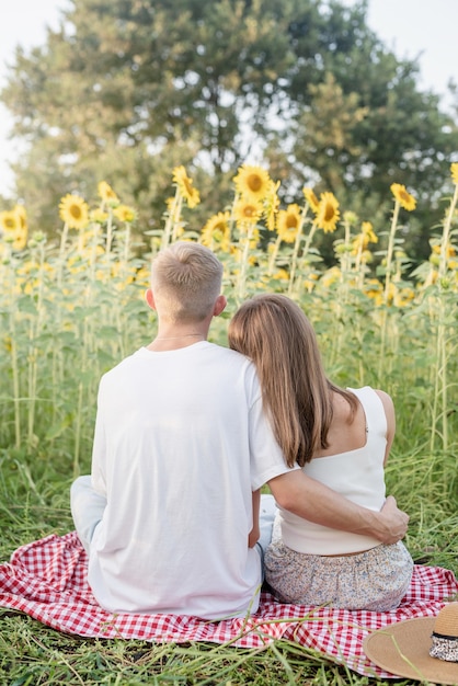 Foto naturaleza otoñal. diversión y mentira. picnic de la joven pareja de adolescentes en el campo de girasol en la puesta del sol, disfrutando del tiempo juntos, vista trasera