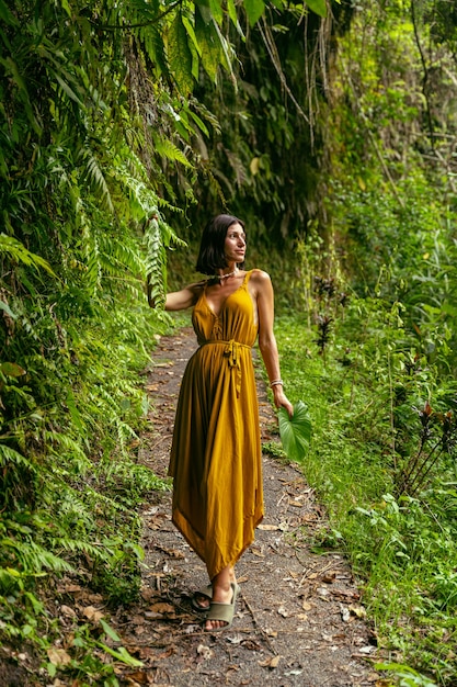 Naturaleza salvaje. Hermosa persona femenina de pie en el camino mientras toma una foto cerca de plantas tropicales