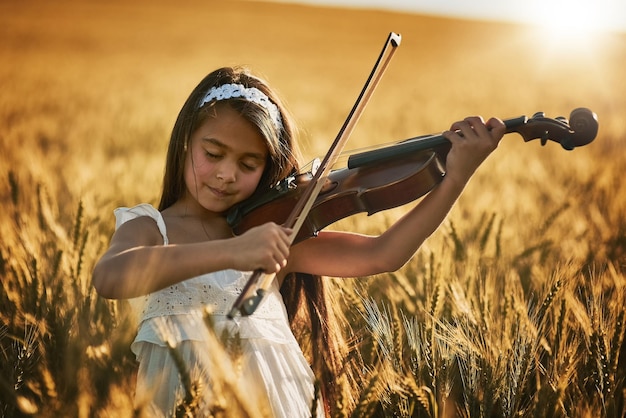 La naturaleza tiene música para aquellos que la escuchan Foto de una linda niña tocando el violín mientras está de pie en un campo de maíz