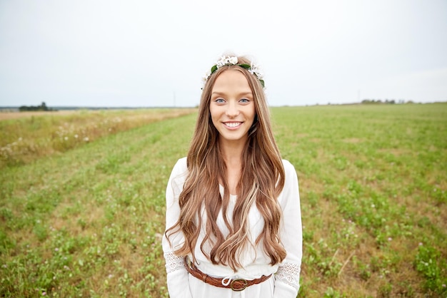 naturaleza, verano, cultura juvenil y concepto de la gente - joven hippie sonriente con corona de flores en el campo de cereal