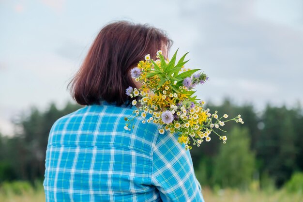 Naturaleza de verano vista trasera de mujer con ramos de flores silvestres