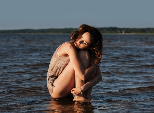 Natureza, beleza, juventude e conceito de estilo de vida saudável. Mulher jovem e atraente seminua em um terno de mergulho posando no contexto do mar. Luz da noite com sombras profundas e mudança de cor