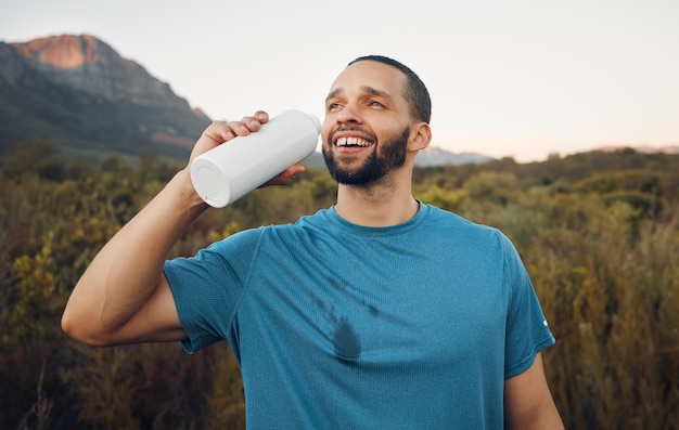 Foto natureza da montanha do corredor e homem bebendo água depois de correr pausa para relaxar e macho da áfrica do sul com líquido refrescante após treino ou exercício no campo de grama para fitness ou saúde