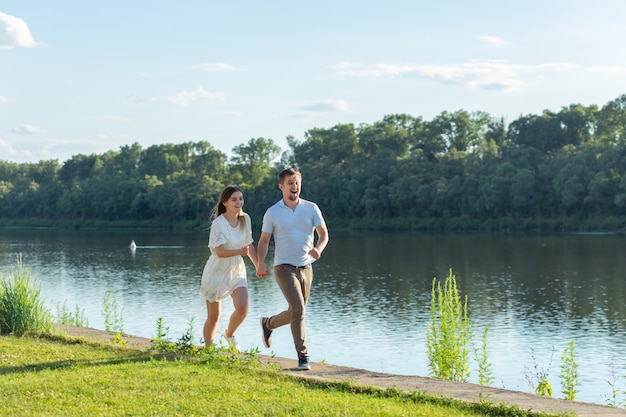 Natureza do verão, relacionamento e conceito de pessoas apaixonadas - casal feliz correndo perto do lago