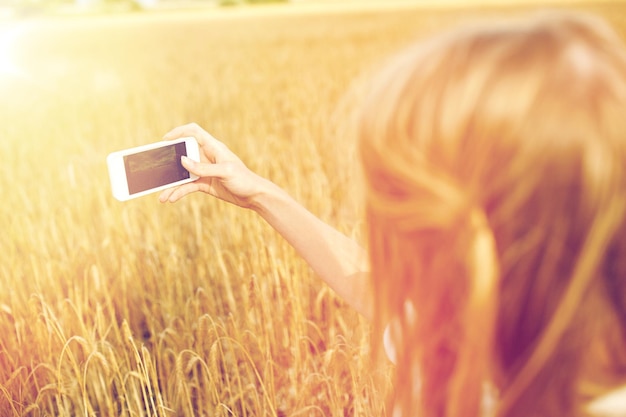 natureza, férias de verão, tecnologia e conceito de pessoas - close-up de jovem com smartphone tirando foto do campo de cereais