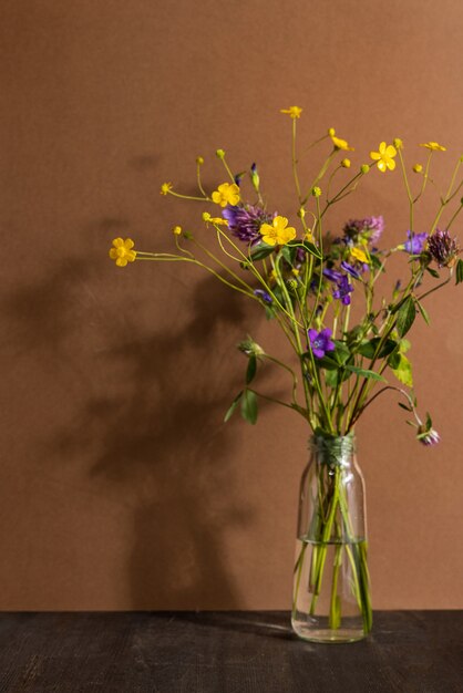 Natureza morta com flores silvestres em frasco de vidro em fundo marrom. Composição moderna e moderna com flores secas, sombras escuras vista lateral