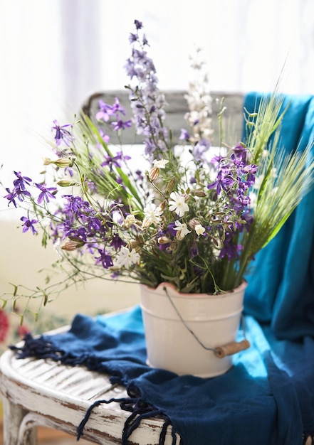 Natureza morta com flores silvestres frescas em um vaso na cadeira vintage