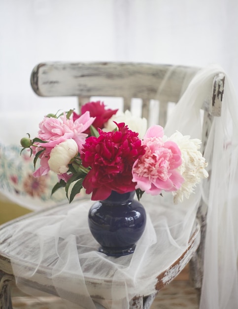 Natureza morta com peônias brancas e rosa em um vaso azul na cadeira vintaje