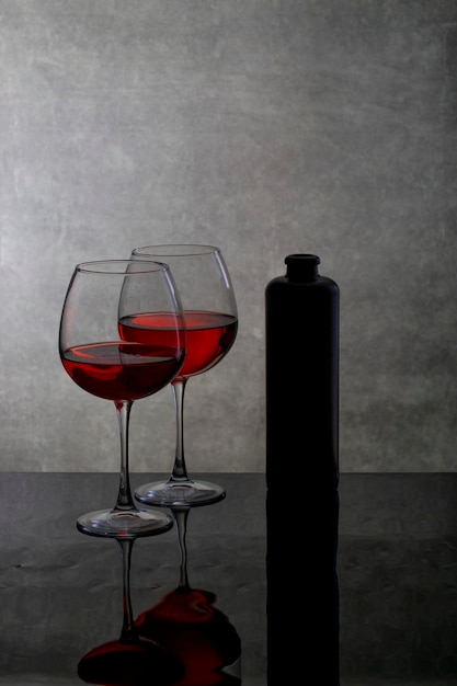 Natureza morta com taças de vinho e uma garrafa em uma superfície reflexiva