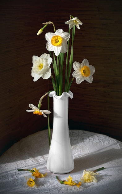 Natureza morta com um buquê de narcisos em um vaso branco em uma mesa redonda com uma toalha de mesa branca.