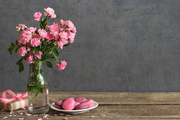 Natureza morta com um lindo buquê de flores rosas, macarons e caixa de presente.