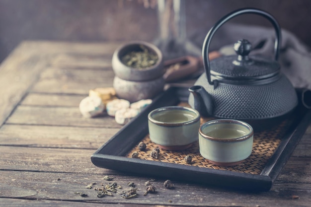 Natureza morta de chá verde japonês saudável em pequenas xícaras e bule sobre fundo escuro