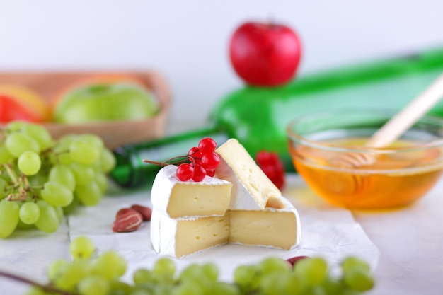 Natureza morta de fruta queijo e uma garrafa verde em um fundo desfocado Queijo creme francês Camembert feito de leite de vaca servido com mel e frutas em pergaminho branco Closeup