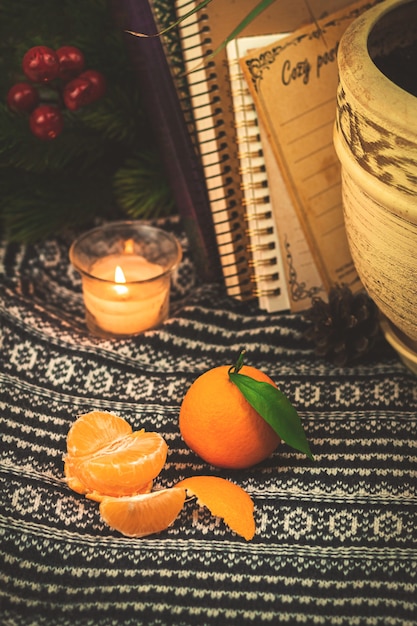 Natureza morta de inverno com tangerinas cítricas em fundo caseiro aconchegante com livros e velas, camisola de malha. Foto de alta qualidade