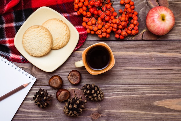 Natureza morta de outono: café, biscoitos, uma manta, um caderno e um lápis na madeira