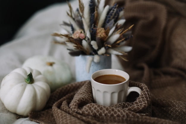 Natureza morta de outono com uma xícara de café com flores e abóboras em uma manta aconchegante