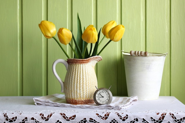 Natureza morta de primavera com cinco tulipas amarelas e um velho despertador no núcleo da casa de mesa