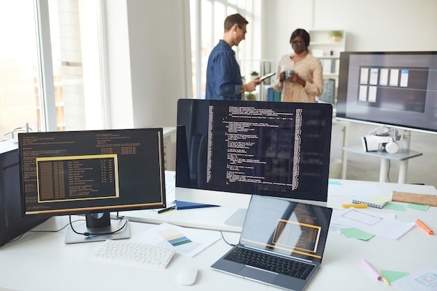 Natureza morta de várias telas de computador na mesa do escritório de desenvolvedores de TI com pessoas em segundo plano, copie o espaço