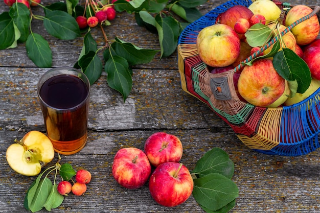 Natureza morta de verão em estilo rústico, maçãs maduras do jardim em uma cesta e deitar sobre a mesa, um copo de suco de maçã. Close-up da foto horizontal.