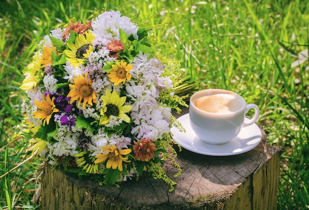 Natureza morta rústica - uma xícara de café da manhã e um buquê de flores silvestres em um velho tronco grande