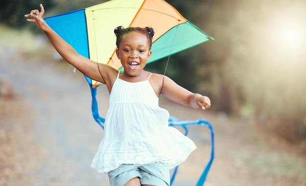 Natureza verão e garota com uma pipa correndo em um parque com um sorriso felicidade de fim de semana e uma criança negra se divertindo ao ar livre desenvolvimento e crescimento de liberdade para criança feliz brincando lá fora