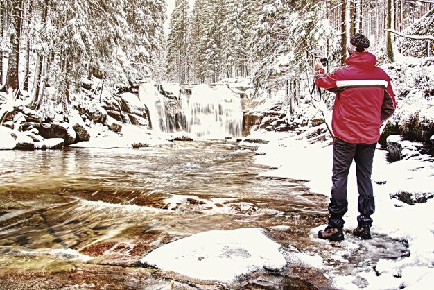 Foto naturfotograf macht ein bild von einer winter-schneelandschaft in einem wald mit wasserfall