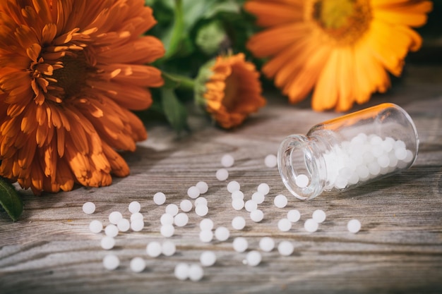 Naturheilkunde Frisch blühende Calendula-Ringelblume und weiße Pillen auf einem Holztisch