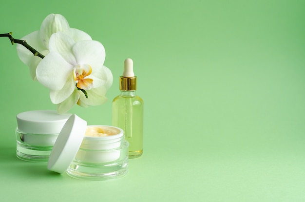 Naturkosmetik Anti-Aging, Anti-Falten, für Frische, Festigkeit der Haut. Creme, Maske, Serum, Flüssigkeit, Öl in der Flasche für die Gesichtspflege, mit Orchideen auf grünem Hintergrund. Banner, Kopierplatz