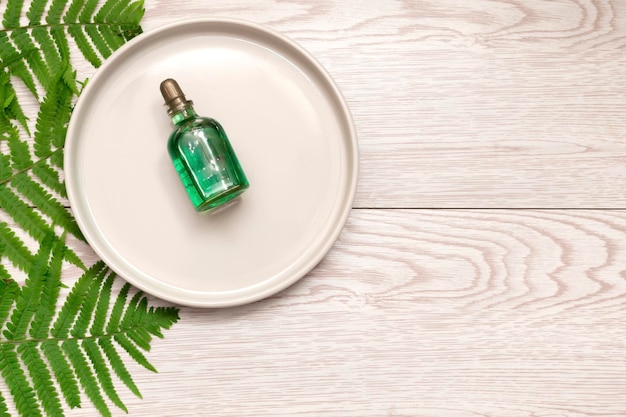 Naturkosmetik Parfüm ätherisches Ölserum in grüner Glasflasche mit Tropfer auf Platte, Holzhintergrund mit grünen Farnzweigen mit Kopierraum. Öko-Ökologie-Schönheitskonzept.