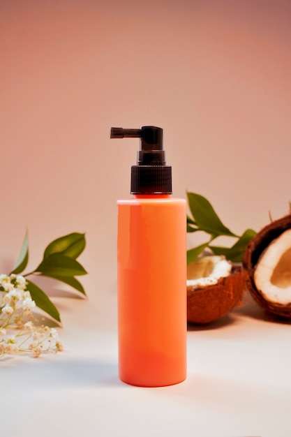 Naturkosmetikflasche für Creme, Gel, Lotion. Kosmetikproduktverpackung, leere rosa Plastikbehälterschablone an der Wand der natürlichen Kokosnuss und der Blätter.