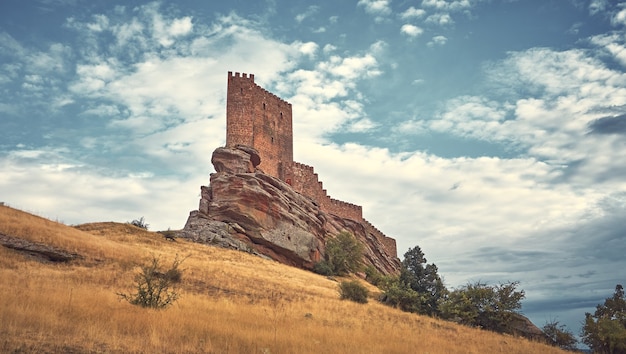 Naturlandschaft mit einer mittelalterlichen Burg auf einem Hügel und den Sonnenstrahlen durch die Wolken