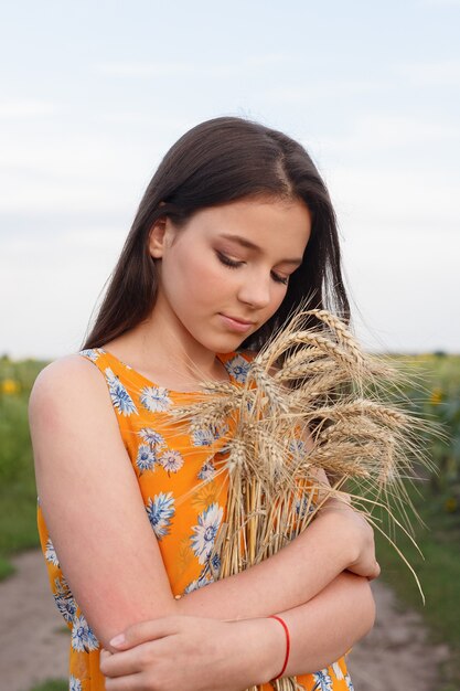 Naturportrait. Nahaufnahme der schönen Frau im Kleid hält Weizenernte in ihren Händen, während sie im gelben Weizenfeld steht.