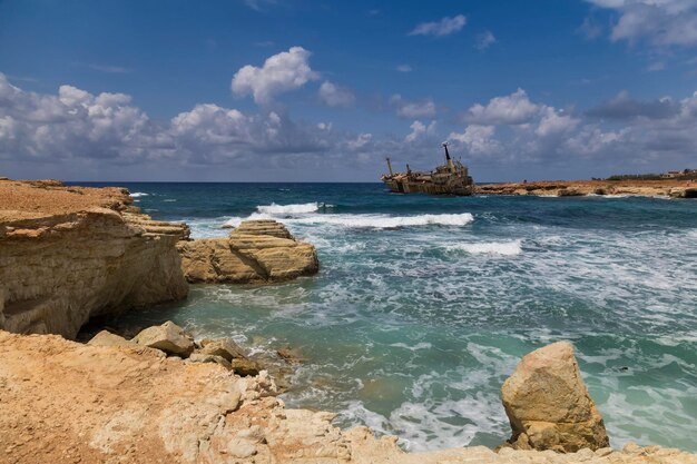 Foto naufrágio navio nas rochas perto do mar turquesa da costa com ondas no fundo do céu nublado penhascos na água a costa mediterrânea perto de paphos chipre paisagem marítima destino turístico