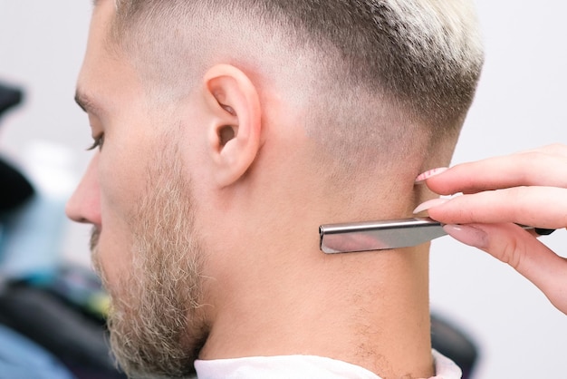 Navaja de afeitar. Proceso de corte de pelo del joven rubio en el salón de peluquería, concepto de peluquería para hombres y niños