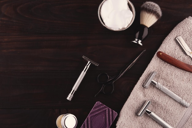 Navalhas vintage, sabão e espuma de escova de barbear em uma tigela sobre um fundo escuro de madeira