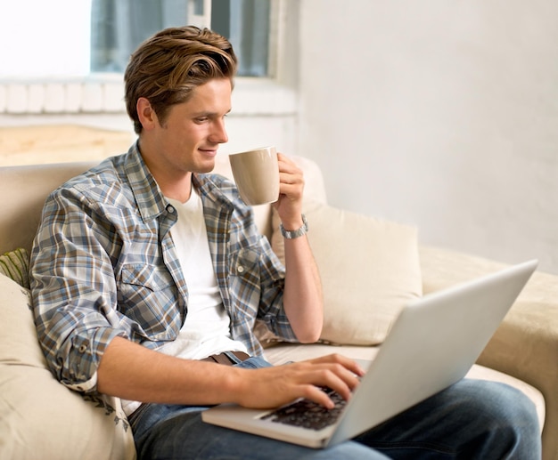 Navegando mientras toma su café de la mañana Foto de un apuesto joven usando su computadora portátil mientras toma un café en casa