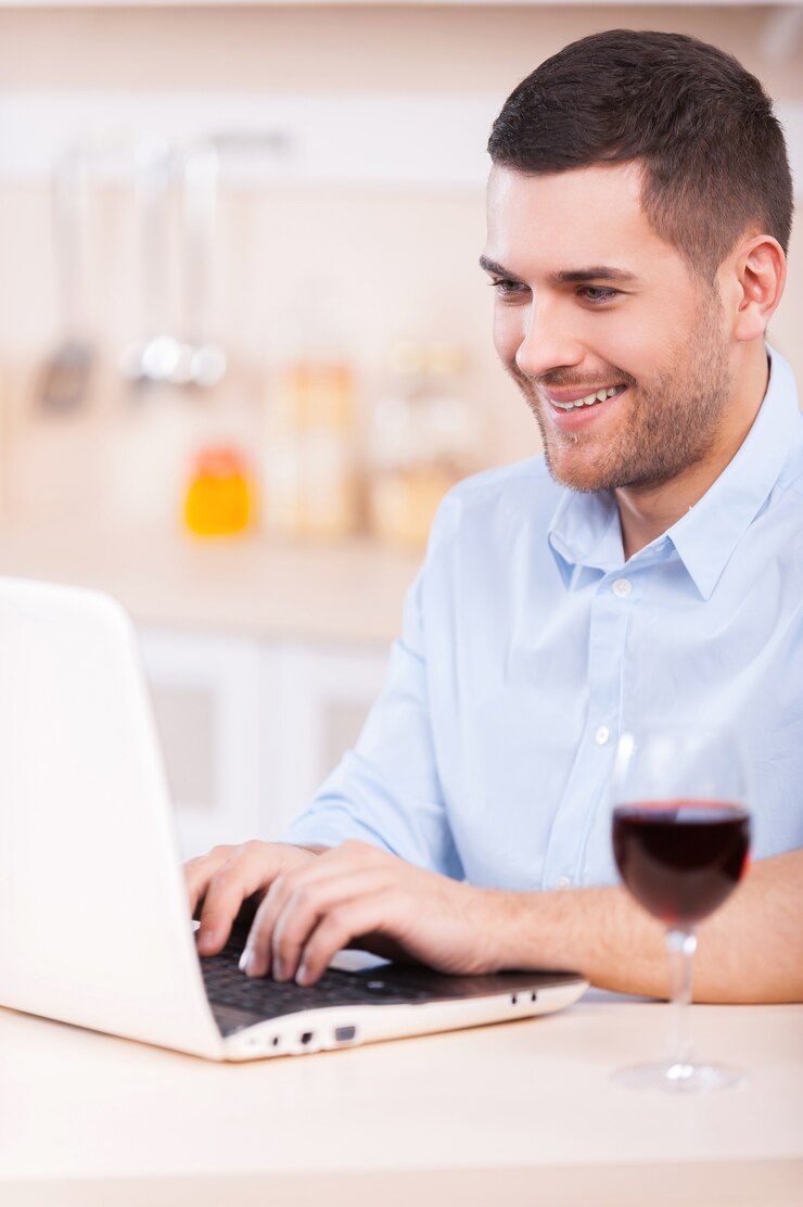 Foto navegando por la red en la cocina. apuesto joven en camisa trabajando en la computadora portátil mientras está sentado en la cocina
