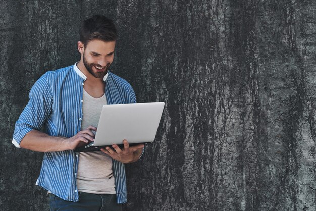 Foto navegar por la red al aire libre apuesto joven en ropa casual elegante trabajando en la computadora portátil mientras