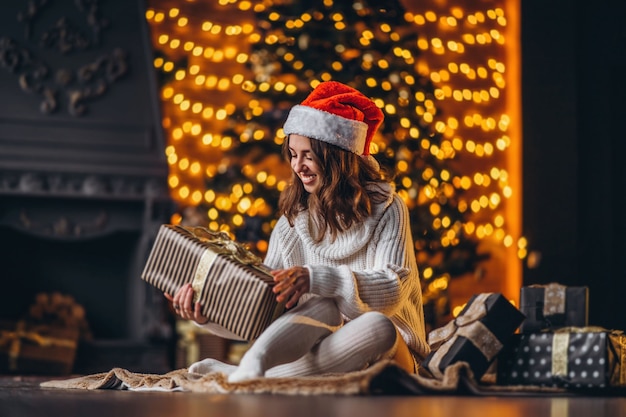 Navidad, año nuevo. Mujer bonita en suéter caliente, calcetines y gorro de navidad, sentada en el suelo