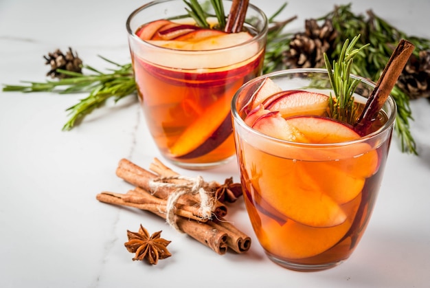 Navidad, bebidas de acción de gracias. Otoño, cóctel de invierno, sangría caliente, vino caliente con especias, manzana, romero, canela, anís. Sobre mesa de mármol blanco. Con conos, romero. Copia espacio