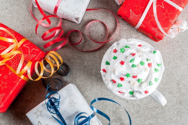 Navidad y. Cajas de regalo de Navidad y taza para café o chocolate caliente, con decoración de crema batida y estrellas dulces, en mesa de piedra gris, vista superior